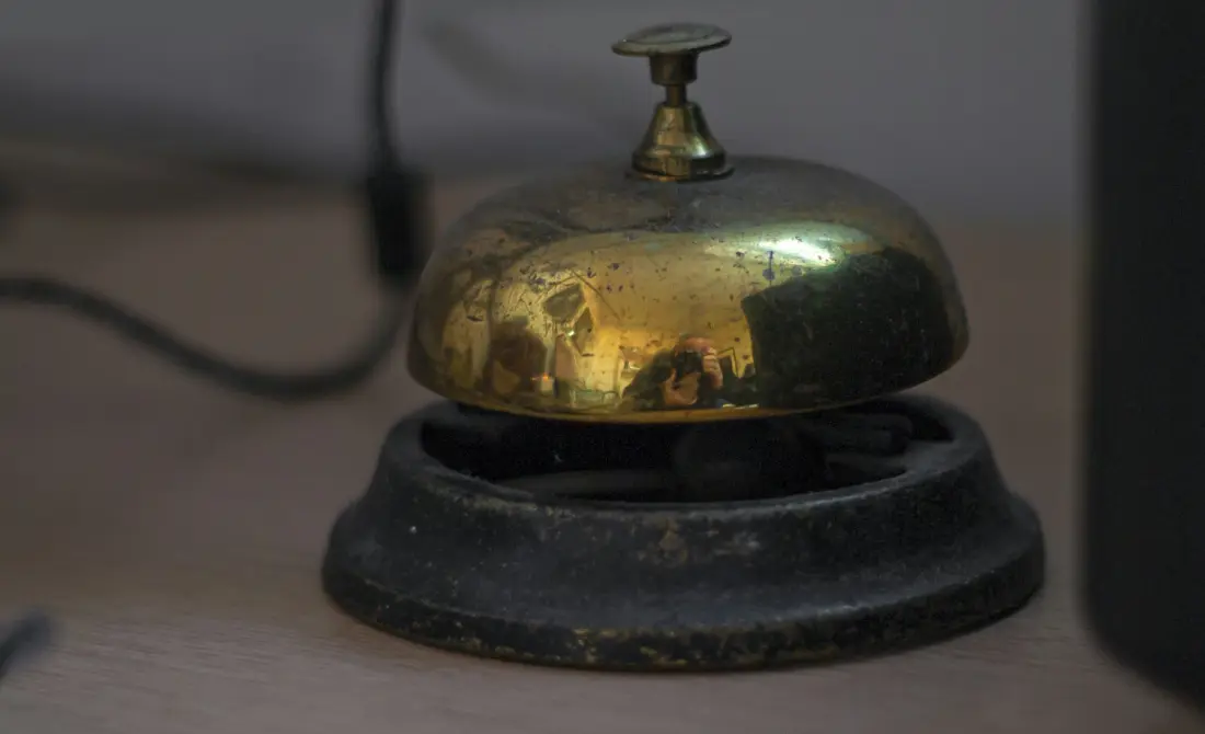A brass service bell resting on a wooden reception desk