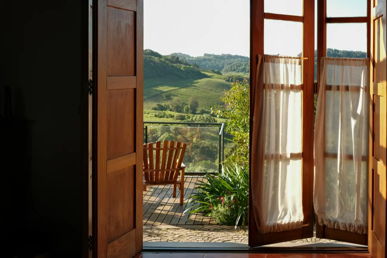 Open wooden doors leading onto a terrace with a chair and a view over green hills