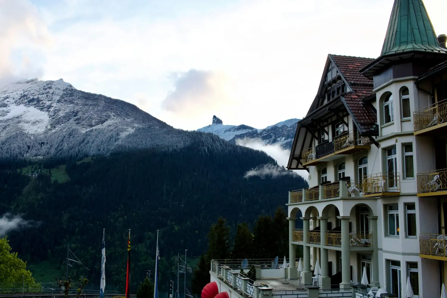 A grand mountain hotel with balconies, snow-capped peaks rising behind it