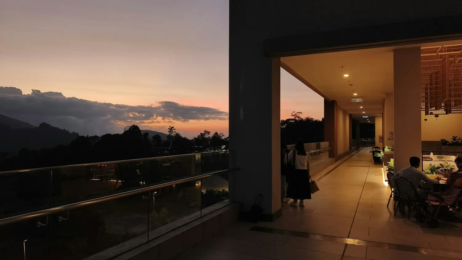 Guests on a hotel terrace at dusk, looking out over hills as the sky turns pink